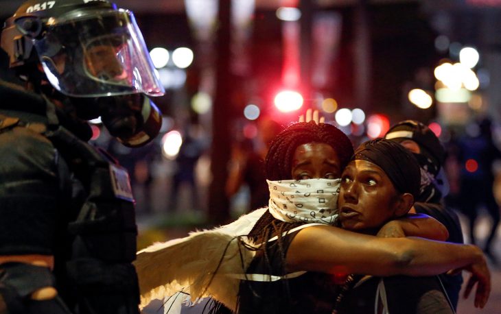 Two women embrace while looking at a police officer in uptown Charlotte, NC during a protest of the police shooting of Keith Scott, in Charlotte, North Carolina, U.S. September 21, 2016. REUTERS/Jason Miczek     TPX IMAGES OF THE DAY